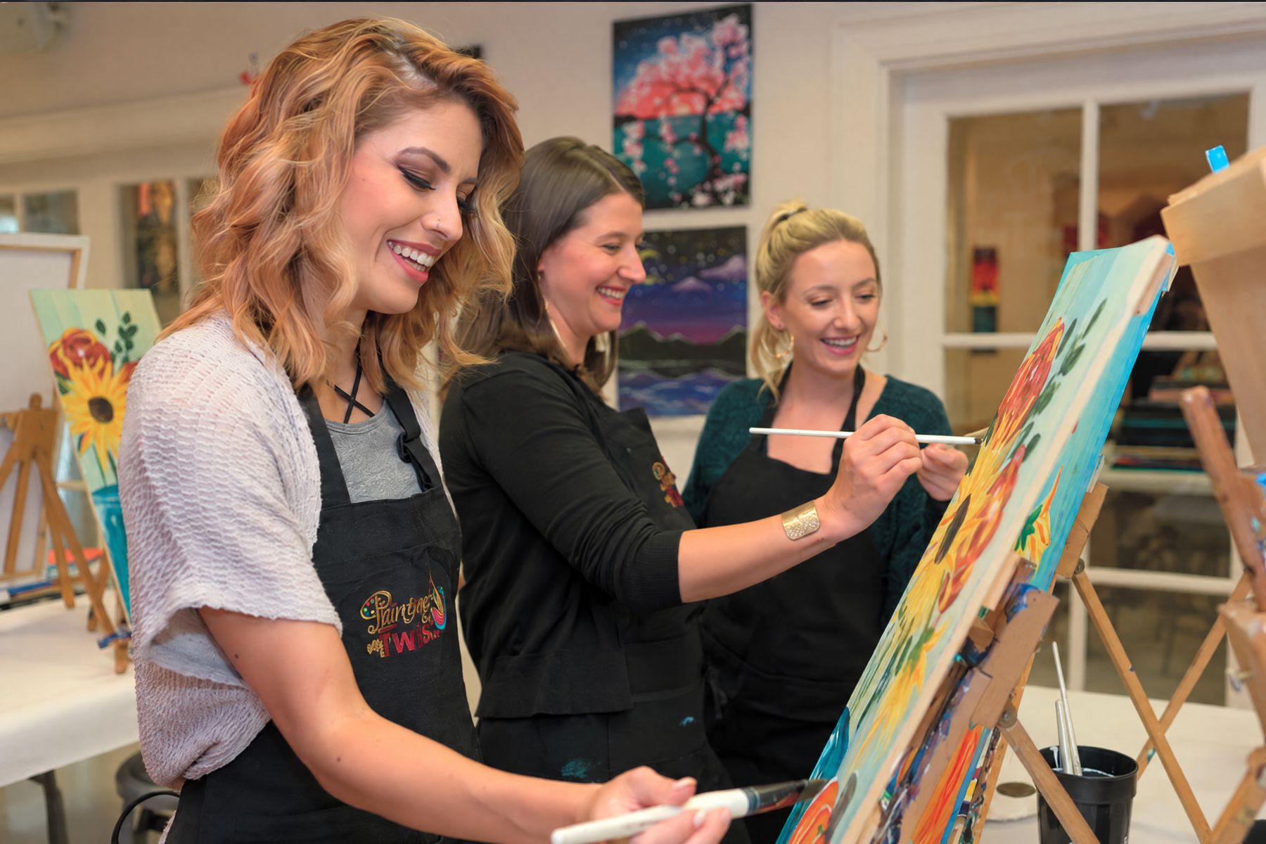 Three women laughing while painting at easels